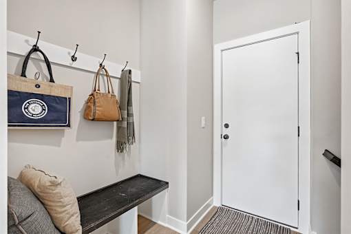 A hallway with a bench, coat rack, and a bag hanging on it.