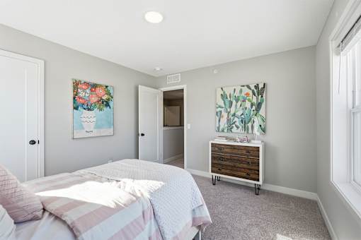 A bedroom with a bed, dresser, and two paintings on the wall.