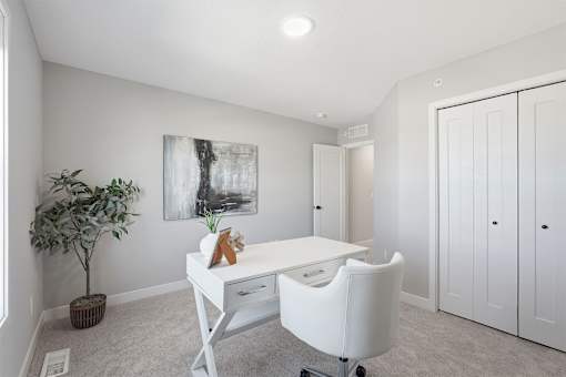 A white desk with a chair and a potted plant in a room with a painting on the wall.