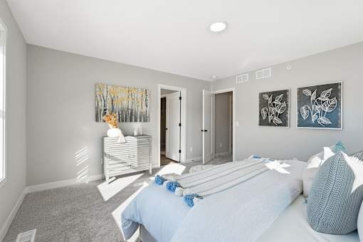 A bedroom with a bed, pillows, and two paintings on the wall.
