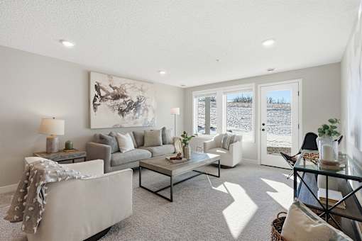 A living room with a grey couch, a glass coffee table, and a large abstract painting on the wall.