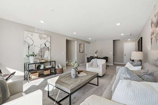A modern living room with a white sofa, a grey couch, a wooden coffee table, and a large abstract painting on the wall.