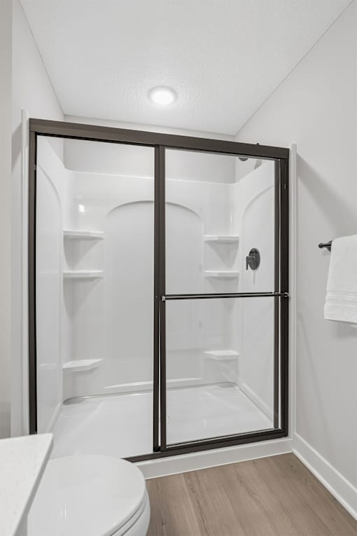 A white toilet is in a bathroom with a walk-in shower.