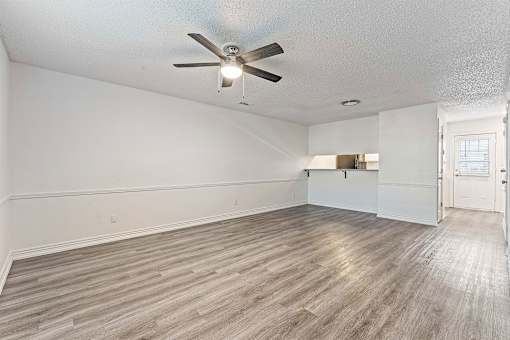 A room with a ceiling fan and light, hardwood floors, and white walls.