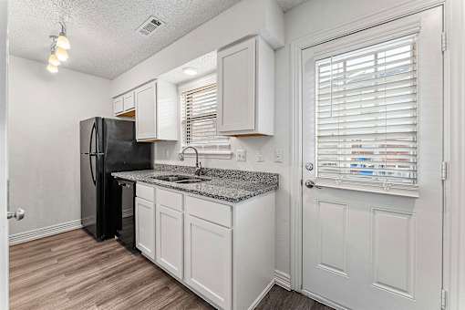 A kitchen with white cabinets and a black refrigerator.