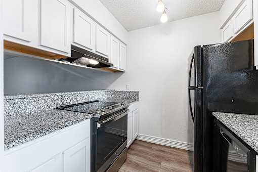 A black fridge sits in a kitchen with white cabinets.