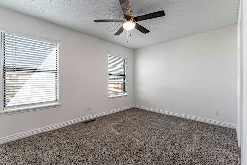 A room with a ceiling fan and two windows.