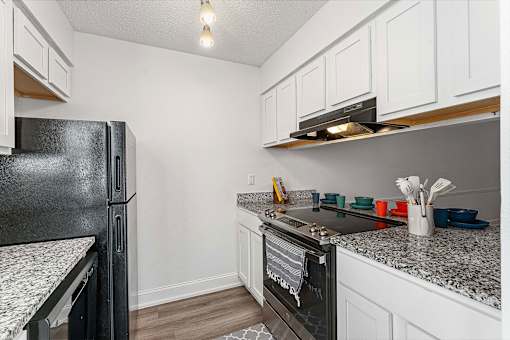 A black refrigerator sits next to a black oven in a kitchen with white cabinets.