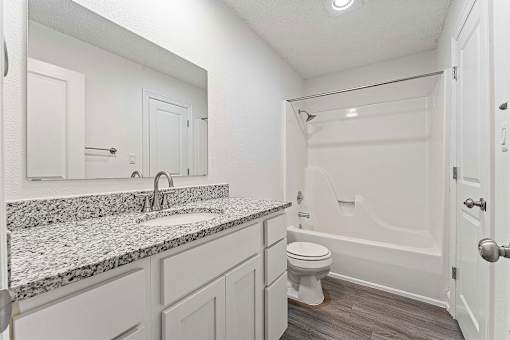 A white bathroom with a marble countertop and a white toilet.