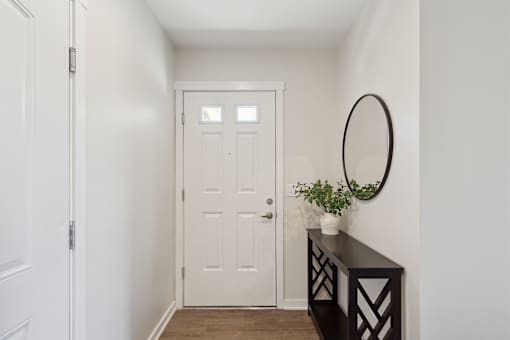A white door is in a hallway with a black console table and a plant on top.