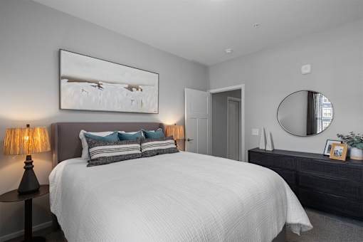 A bedroom with a large bed, a painting on the wall, and a round mirror above a dresser.