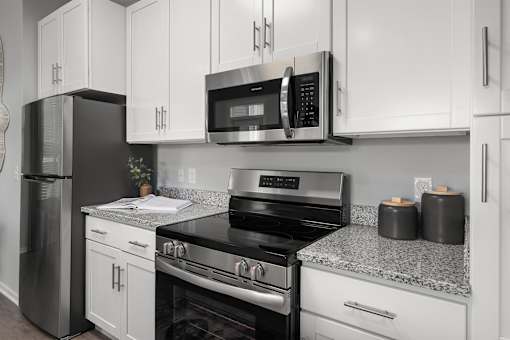 A black refrigerator and oven in a kitchen with white cabinets.