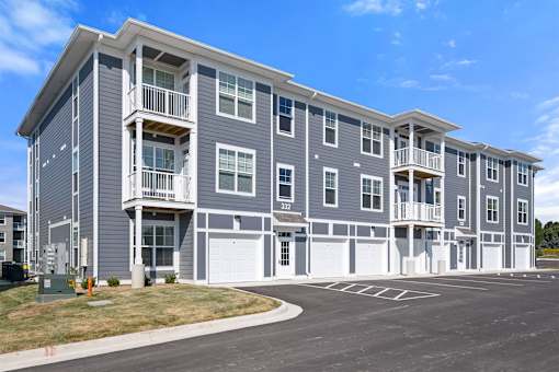 A large grey apartment building with a parking lot in front.