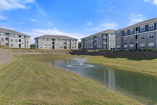 A large grassy area with a pond and apartment buildings in the background.