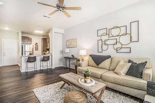 A living room with a beige couch, a white rug, and a ceiling fan.
