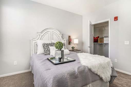 A bedroom with a bed, pillows, a tray with a plant and candles, and a door leading to a kitchen.