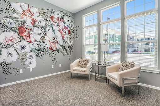Two chairs are placed in front of a wall with a floral mural.