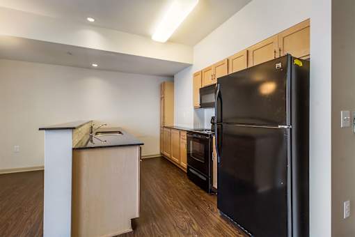 A kitchen with a black refrigerator and wooden cabinets.