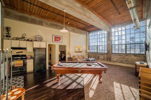 A billiard table is in the middle of a room with a wooden floor and a large window.