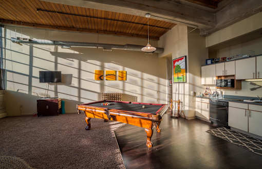 A pool table in a room with a TV and a kitchen area.