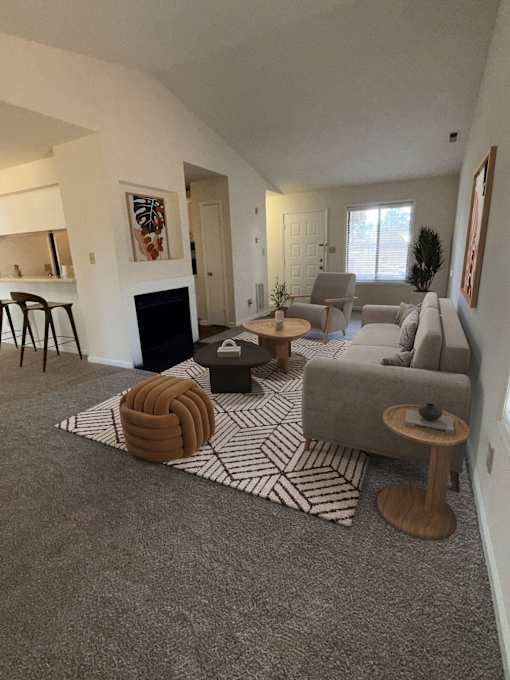 A living room with a grey carpet and a fireplace.