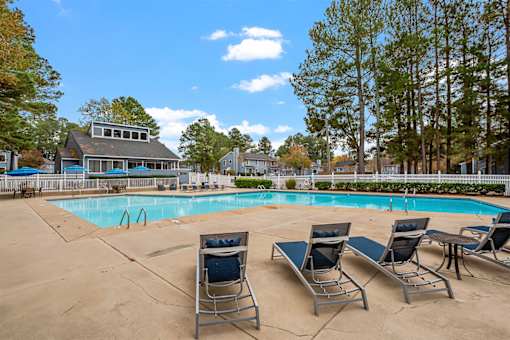 A pool surrounded by trees and chairs.