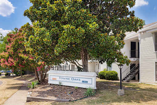 A sign that says Towne Oaks is in front of a tree.
