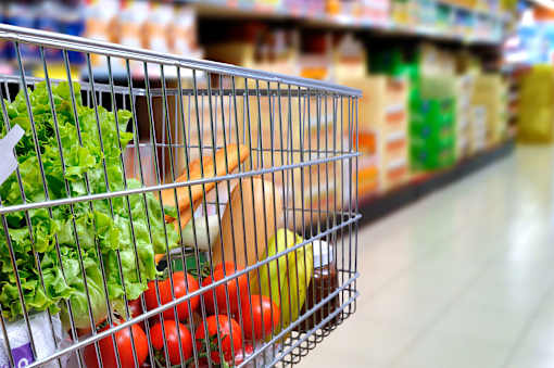 A shopping cart filled with vegetables in a grocery store.