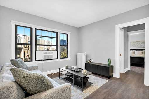 A living room with a grey couch, a coffee table, and a large window with a view of a building.