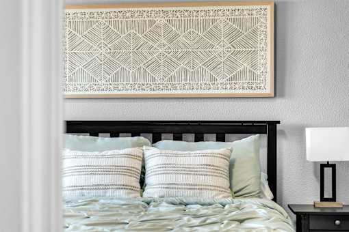 A bed with a black headboard and a white pillow with a geometric patterned artwork above it.