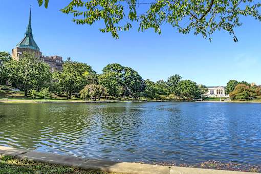 A serene lake surrounded by lush greenery and a building with a green spire in the background.