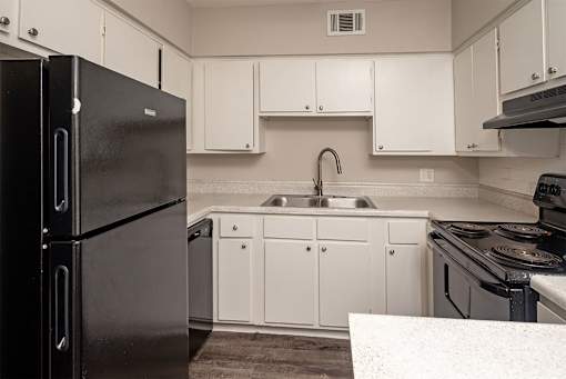 A black refrigerator stands in a kitchen with white cabinets and a sink.