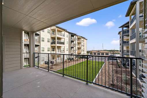 A balcony with a black railing overlooks a grassy area and other buildings.