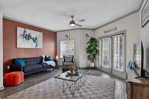 A living room with a grey sofa, a glass coffee table, a TV, and a painting on the wall.