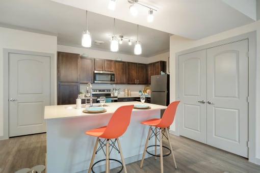 a kitchen with white cabinets and a white island with two orange chairs