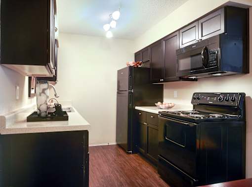 A kitchen with black appliances and brown flooring.