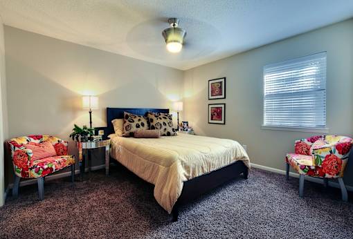 A bedroom with a bed, two chairs, and a nightstand.
