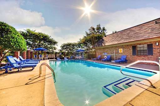 A sunny day at the pool with blue lounge chairs and a building in the background.
