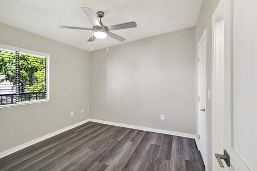 A room with a ceiling fan and a window with blinds.