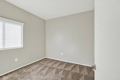 A room with a carpeted floor and a window with blinds.