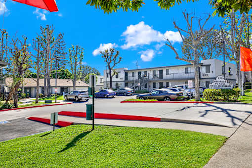 A sunny day at the Heritage Apartments with cars parked and trees in the background.