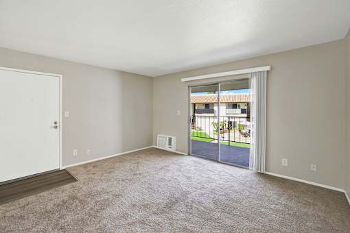 A room with a carpeted floor and a sliding glass door leading to a patio.