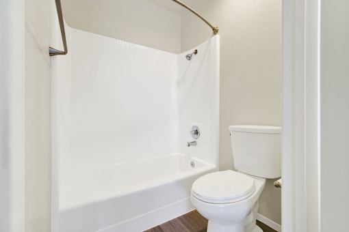 A white toilet is in a small bathroom with a white tub.