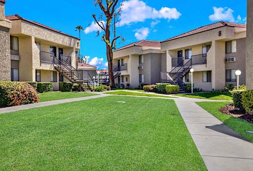 A sunny day at a well-kept apartment complex with green lawns and clear skies.