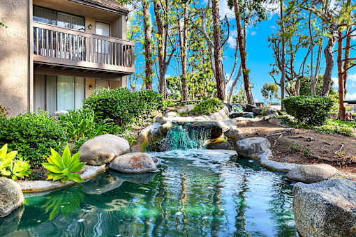 A small waterfall in a garden with a building in the background.