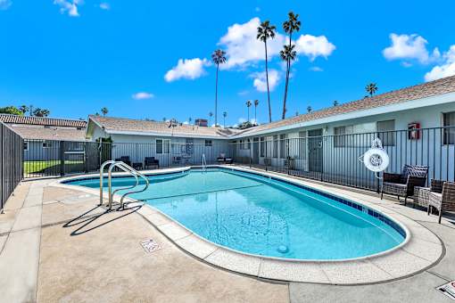 A pool surrounded by a black fence with a chair and palm trees in the background.