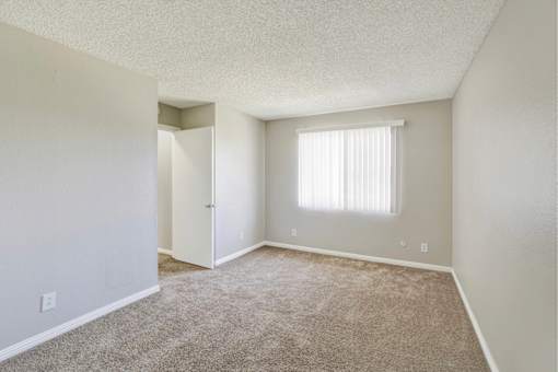 Spacious empty bedroom with carpet and window at ELEVATE Apartments HOMES, Placentia, CA