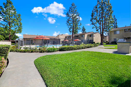 Fenced pool area with walking path and greenery at ELEVATE Apartments HOMES, Placentia, CA