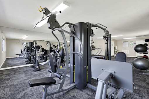A gym with a variety of equipment including a leg press machine at THE STREAMS Apartments, Fullerton, 92831