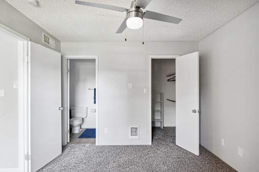 A white room with a ceiling fan and a toilet in the corner.